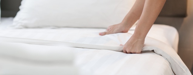 A member of the hotel hospitality staff makes up a bed featuring crisp, white, 100 percent cotton luxury bedsheets.