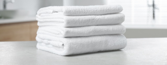 A stack of crisp, white terrycloth towels on a hotel bathroom counter.