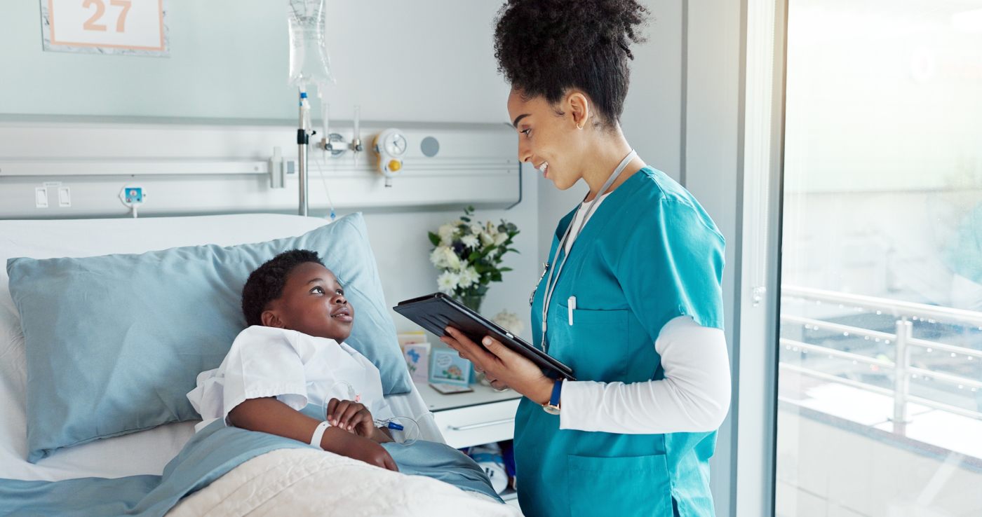 A young boy in a hospital bed talking to a nurse.