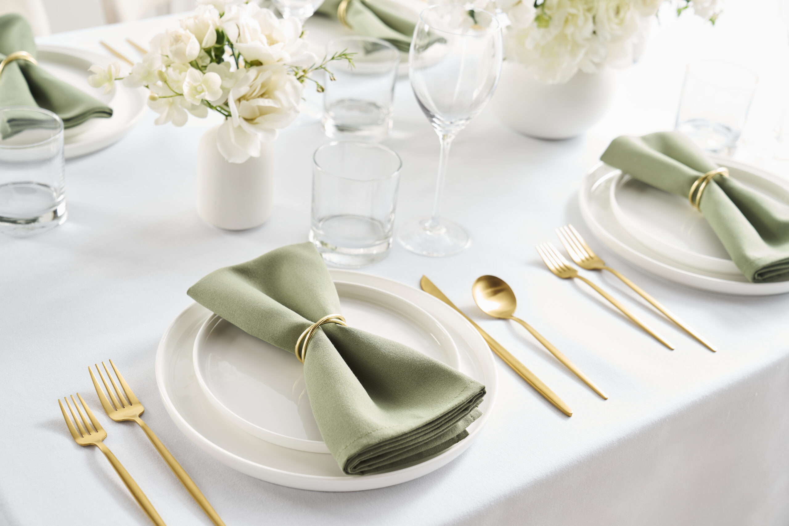 Elegant table setting with gold flatware and green Reigel napkins.