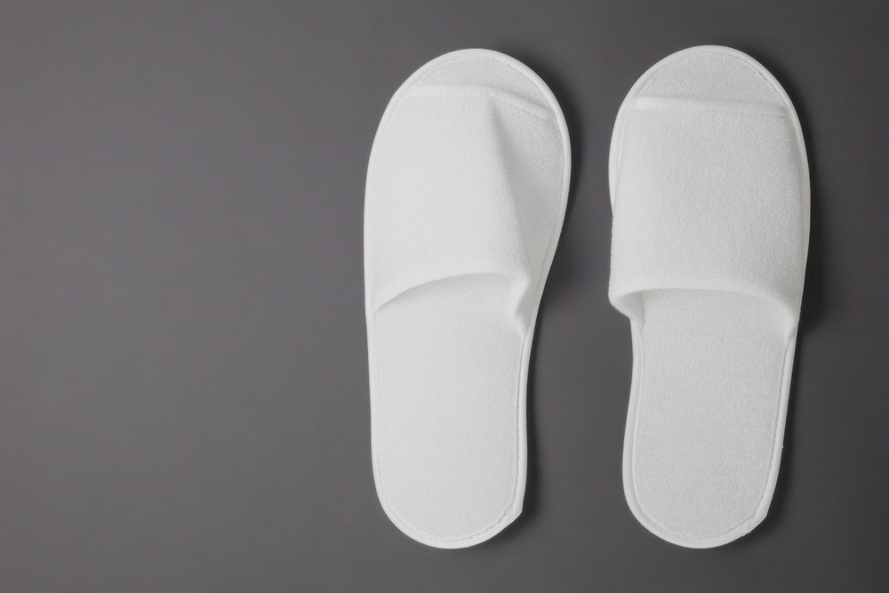A pair of new terry slippers against a gray background.