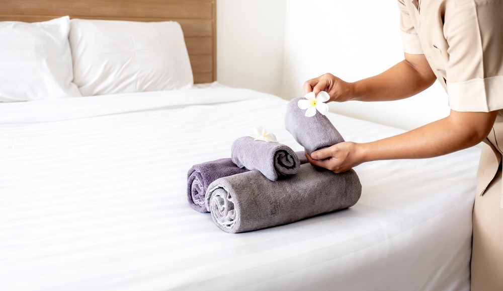 A hotel maid styles a bed using bulk hotel linens.