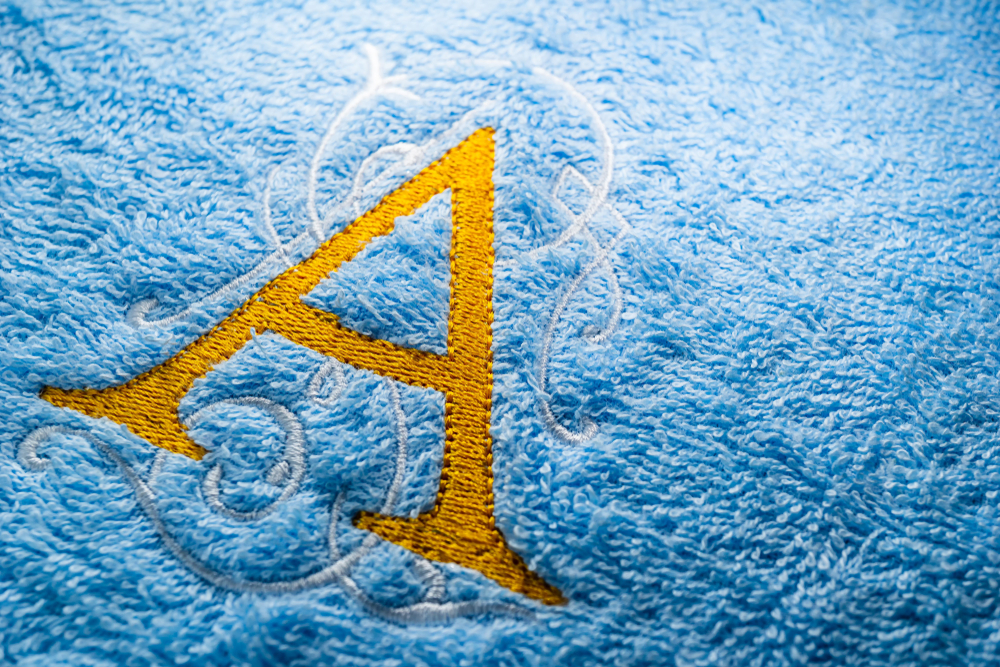 A golden, filigreed monogrammed letter A on a pale blue hotel towel.