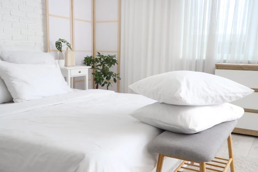 A stack of soft pillows placed atop a small wooden rack at the foot of a big hotel room bed.